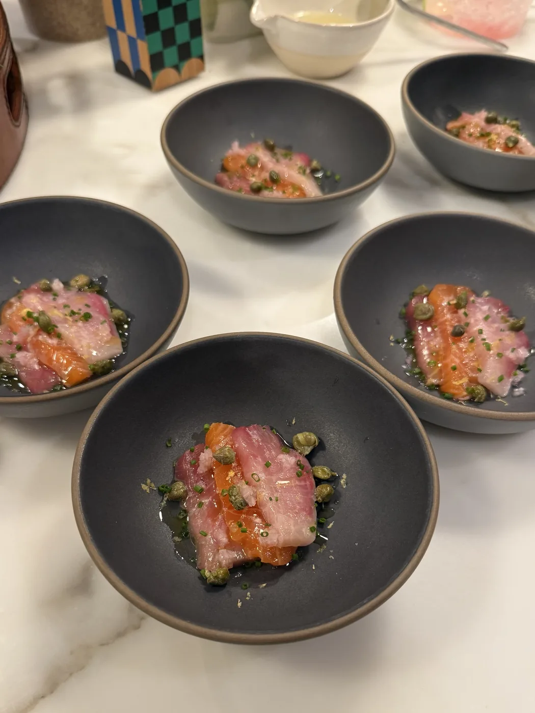 Sicilian crudo plated in dark bowls with capers and herbs