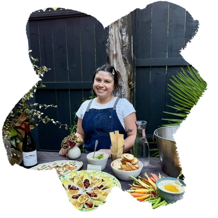 Tash smiling behind an outdoor table set with colorful platters and small bites